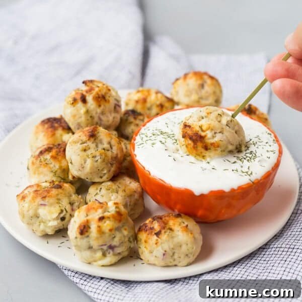 Crispy Air Fryer Italian-Style Meatballs Recipe 14 A plate of baked Greek turkey meatballs next to a bowl of white dipping sauce, with one meatball being dipped using a skewer.