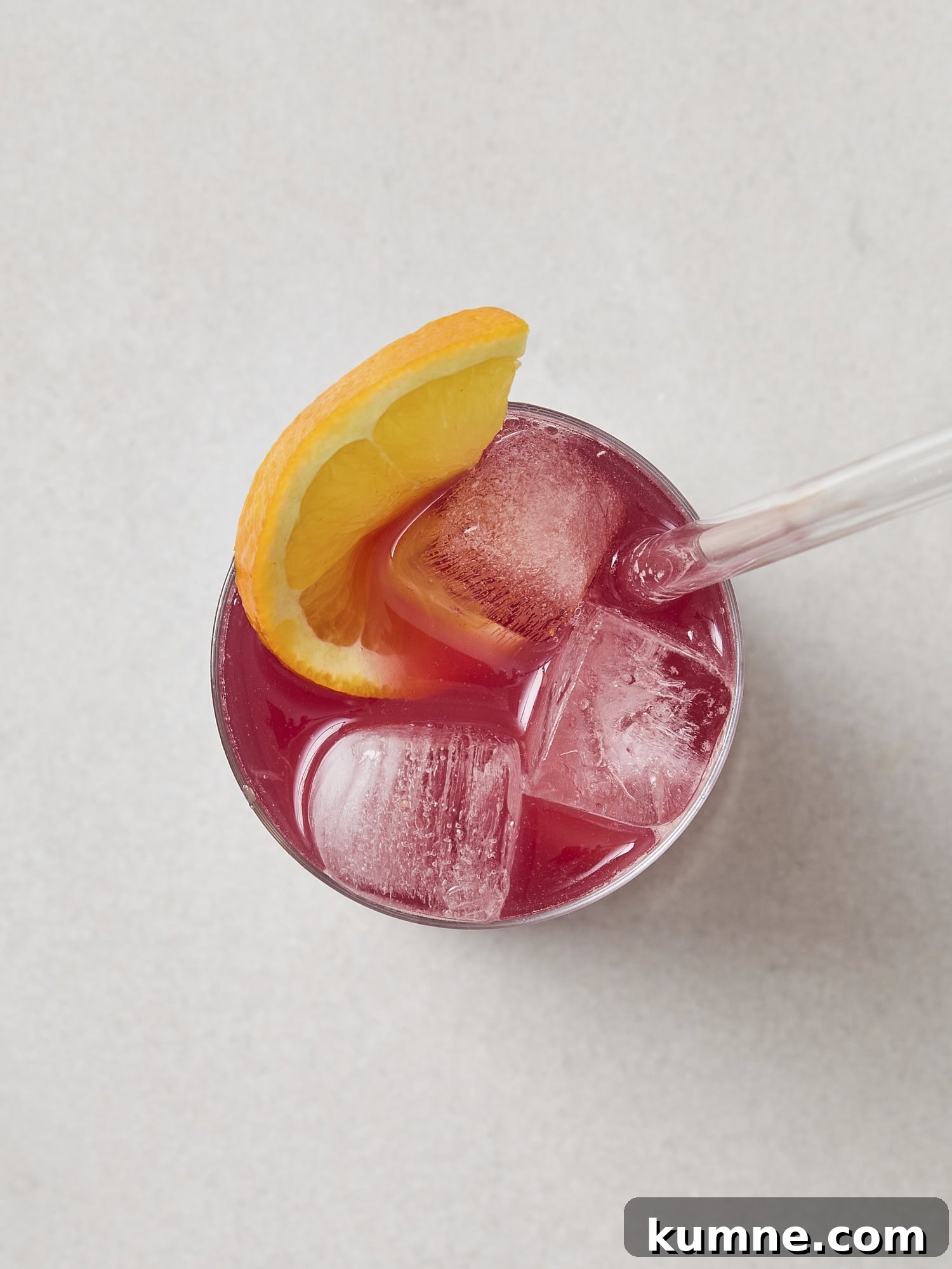 Glass with ice with pink mocktail liquid and orange slice on top.