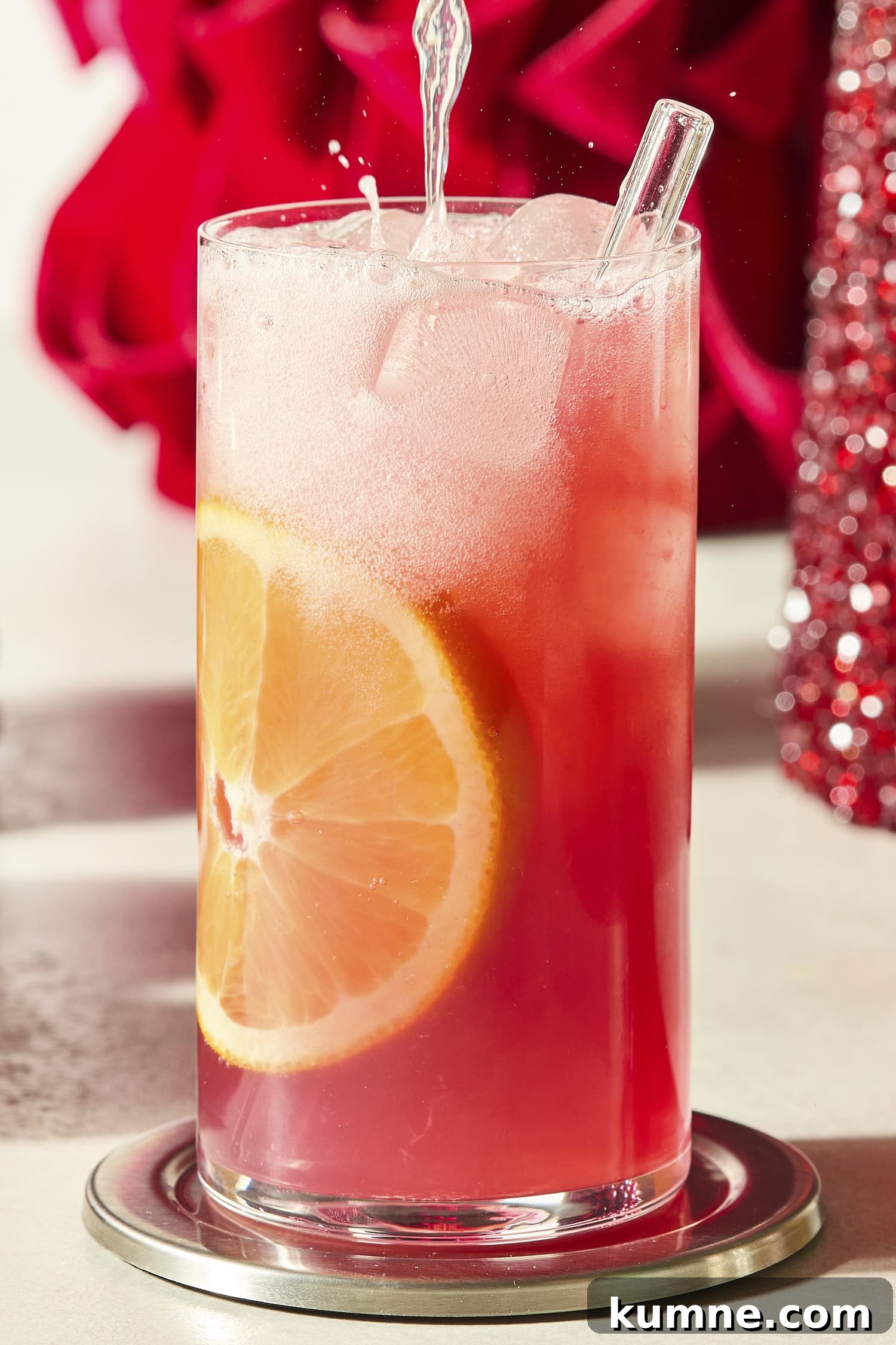 Liquid being poured into a tall cocktail glass filled with cranberry orange mocktail.
