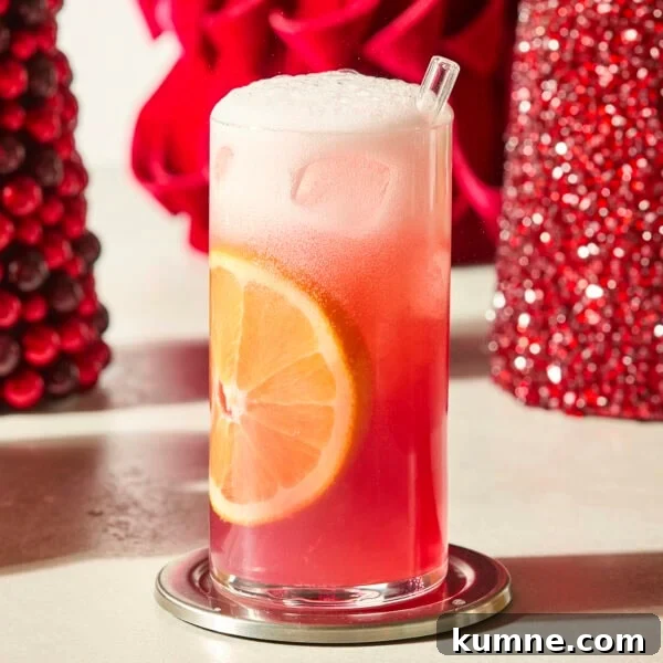 Tall glass with cranberry orange mocktail and an orange slice in the side.