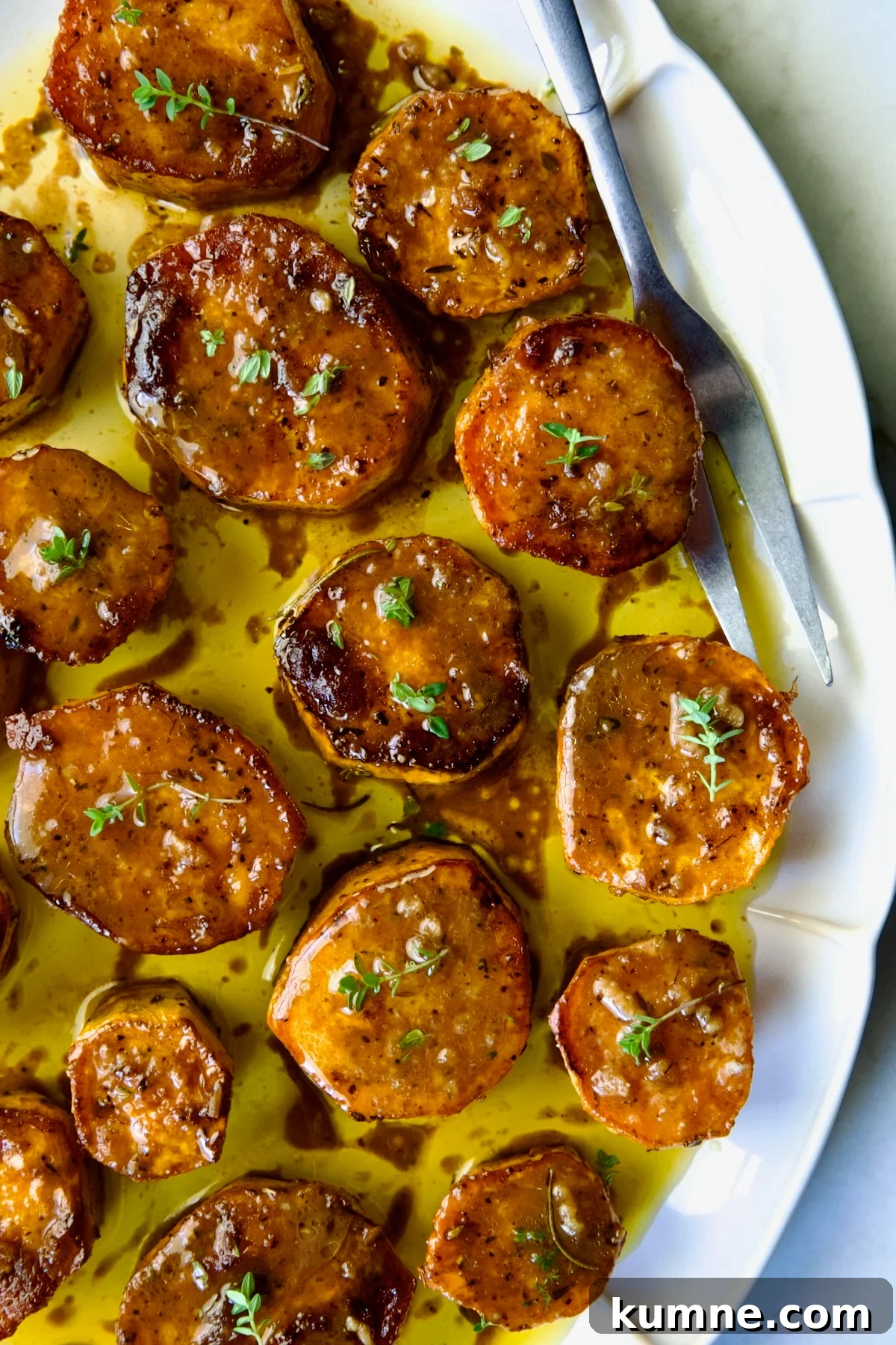 Fondant Sweet Potatoes garnished with fresh thyme on white oval platter.