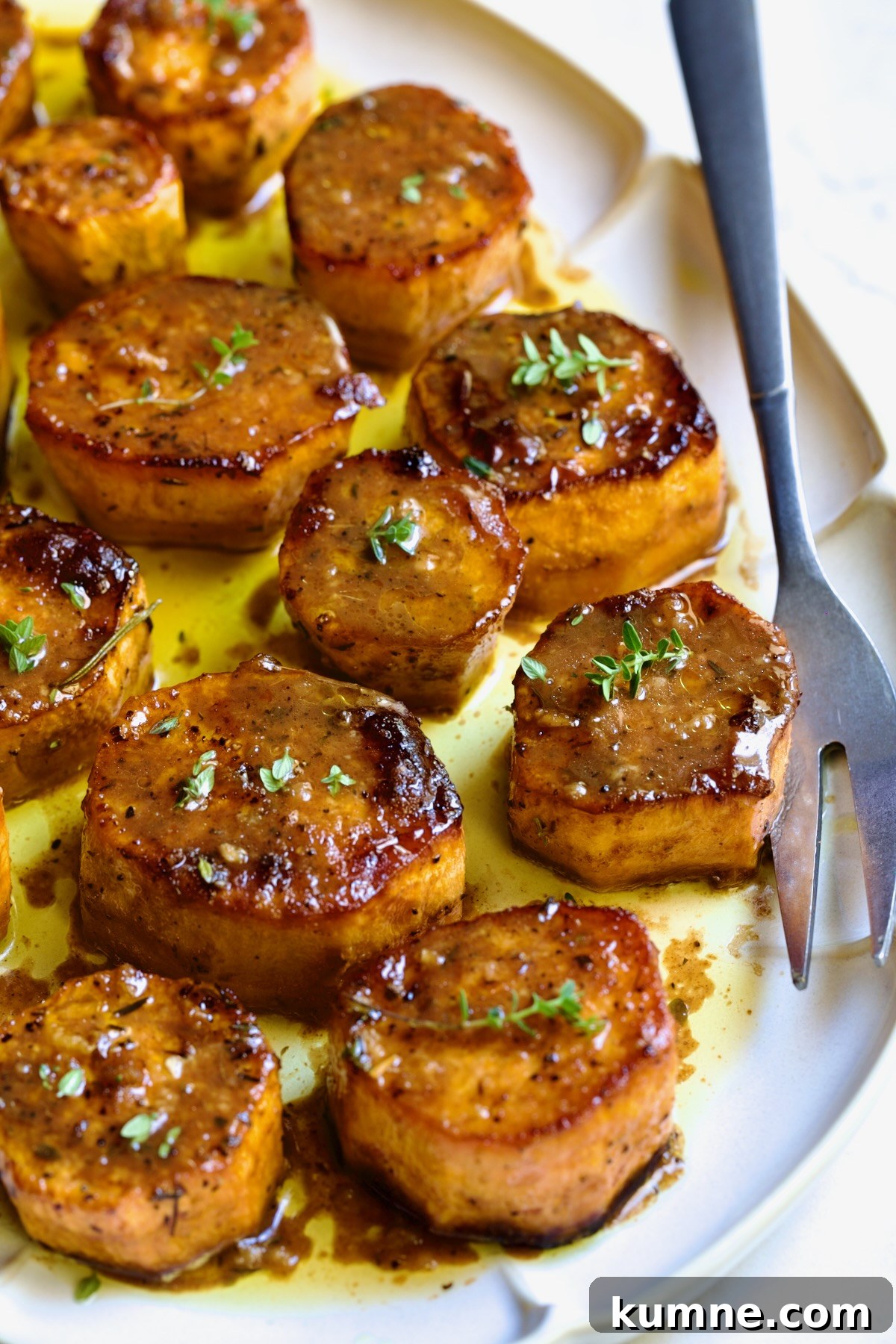 Fondant Sweet Potatoes garnished with fresh thyme on white oval platter.