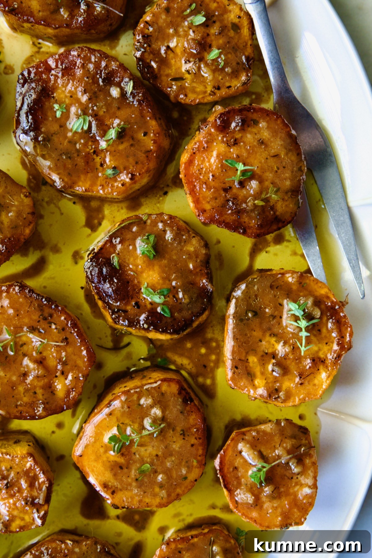 Fondant Sweet Potatoes garnished with fresh thyme on white oval platter.