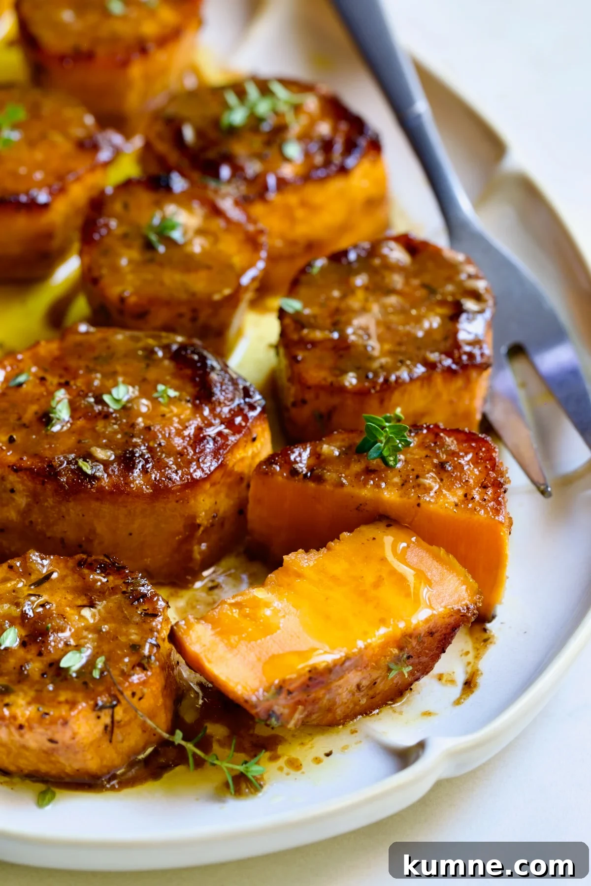 Fondant Sweet Potatoes garnished with fresh thyme on white oval platter with one cut in half.