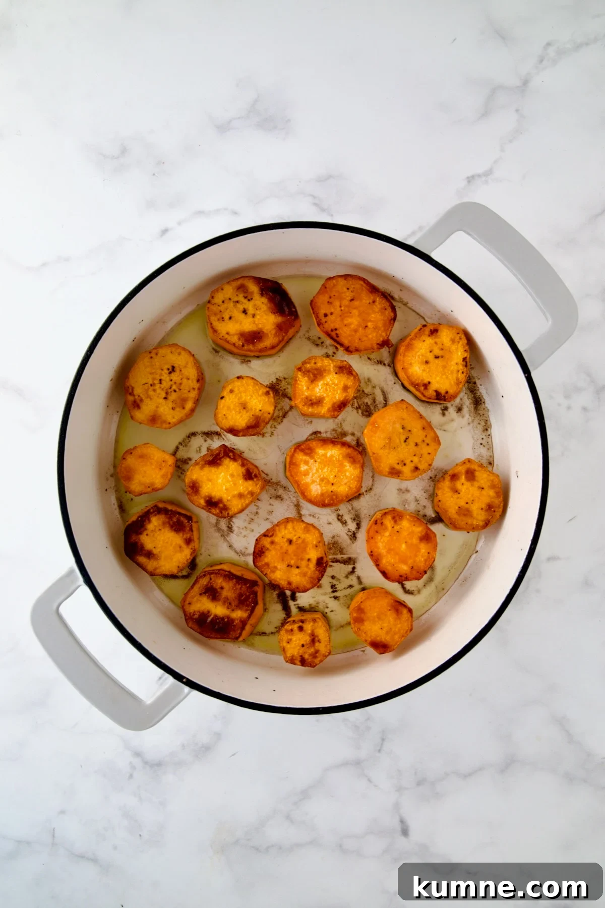 Rounds of sweet potatoes in white enamel cast iron skillet after being browned.
