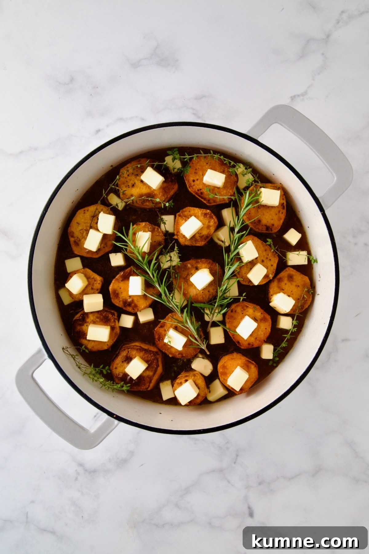 Butter and herbs added to browned sweet potato rounds in white enamel cast iron skillet.