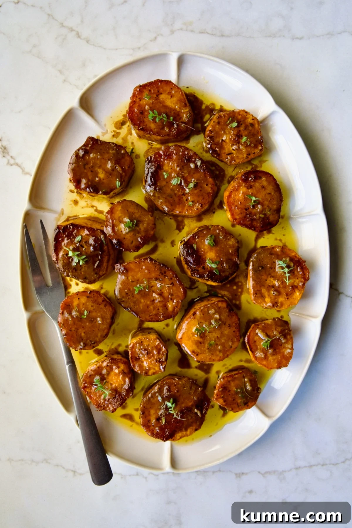 Fondant Sweet Potatoes garnished with fresh thyme on white oval platter.