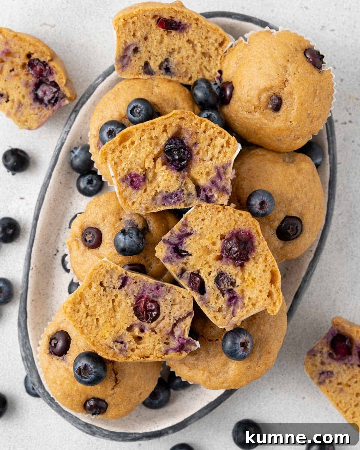 a dish with many muffins and a couple of muffins cut in half with fresh blueberry garnish.