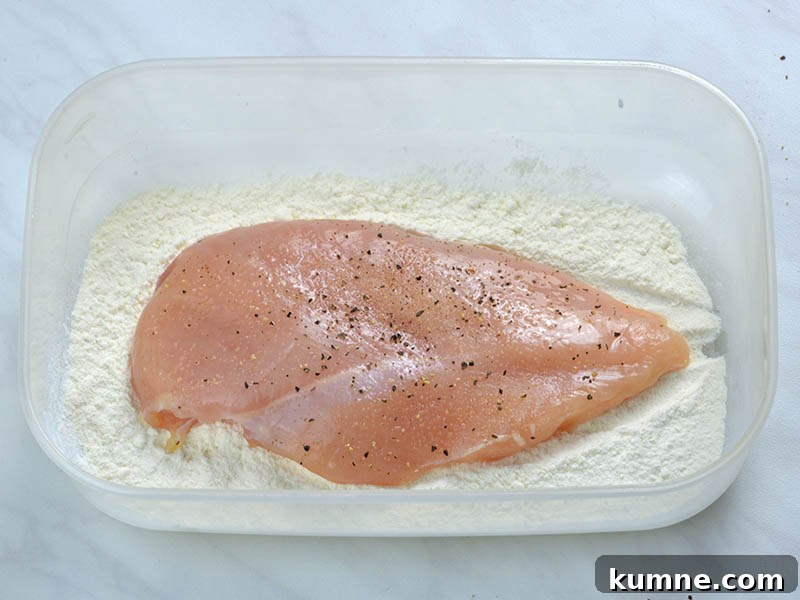 Chicken breast in half with season with salt, freshly ground black pepper and garlic powder laying on flour.