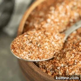 Spoonful of turkey rub resting on the edge of a wooden bowl full of the same rub.