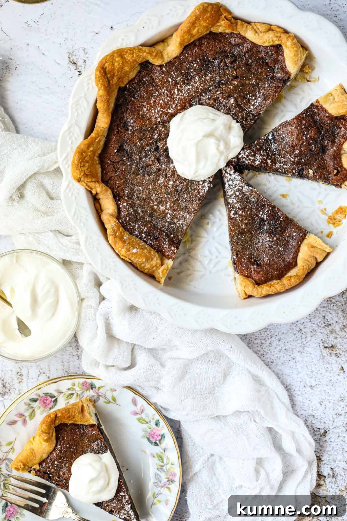 A sliced chocolate chess pie in a white pie dish topped with whip cream.