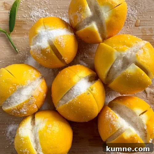 Fresh lemons on a cutting board with slits cut in them filled with kosher salt.