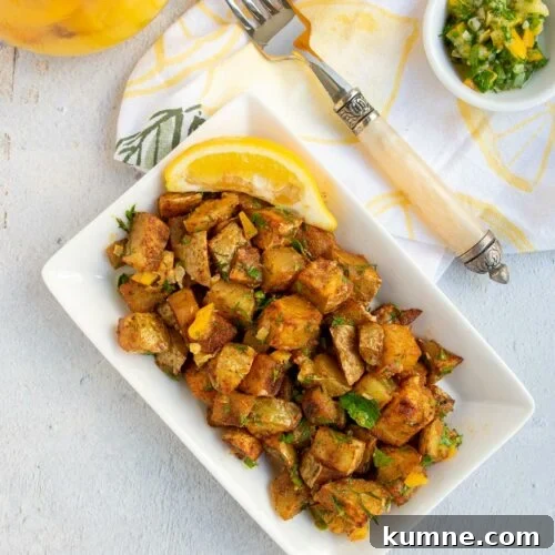 Roasted harissa potatoes on a white plate with a small bowl of gremolata and a lemon napkin.