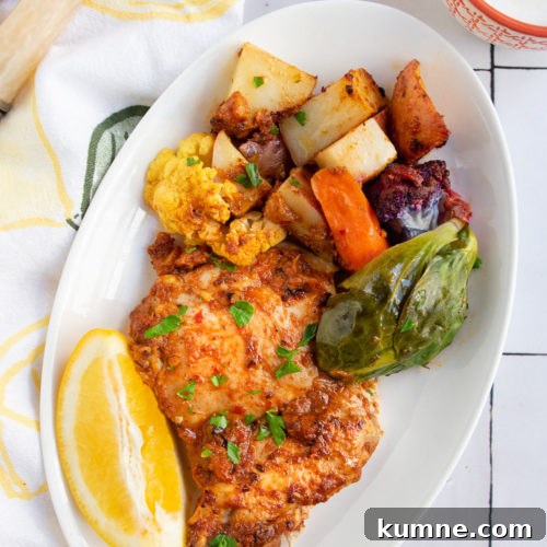 Harissa chicken and vegetables on a white plate with a slice of lemon.