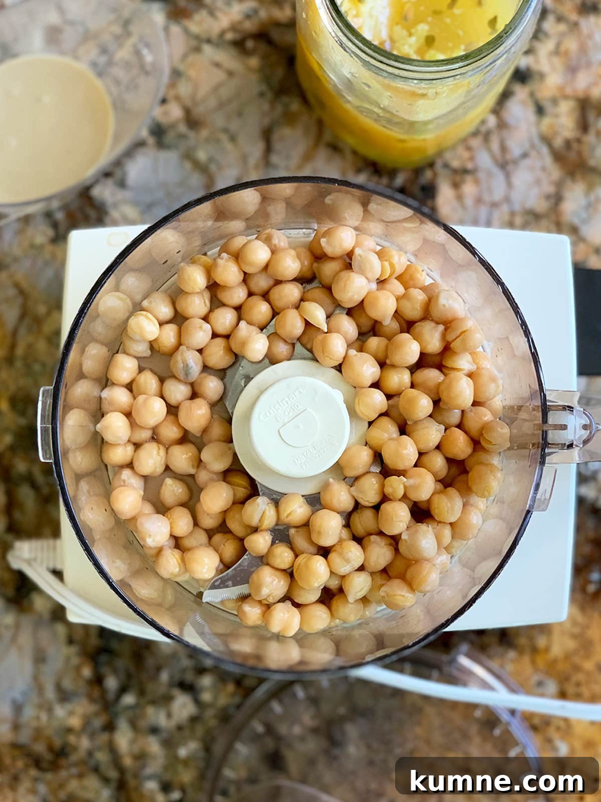 Preserved lemon hummus chickpeas in processor with tahini and lemons nearby.