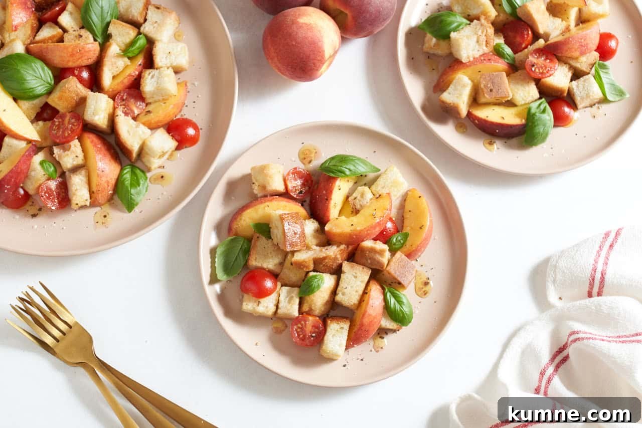 Three pink plates of peach panzanella salad topped with fresh basil leaves, gold forks are on the left, a red and white striped towel is on the right.