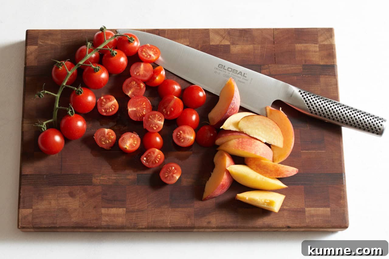 Sliced peaches and cherry tomatoes on a wooden cutting board with a knife.