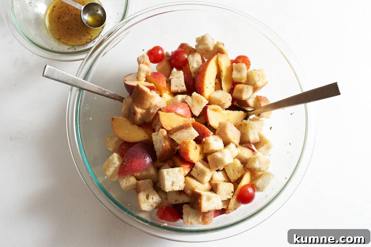 Bread cubes, peaches, and tomatoes tossed in a salad dressing in a large mixing bowl.