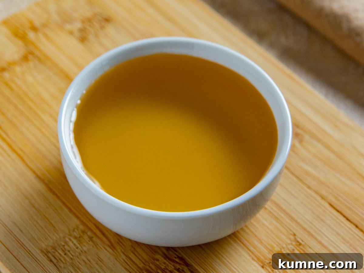 Agave nectar in a small white bowl on a wooden cutting board.
