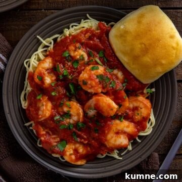 Shrimp Marinara spaghetti on a brown plate with a dinner roll on the side.