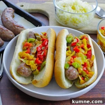 brats in buns topped with red, green, and yellow bell pepper strips on top. Sauerkraut in bowl in background.