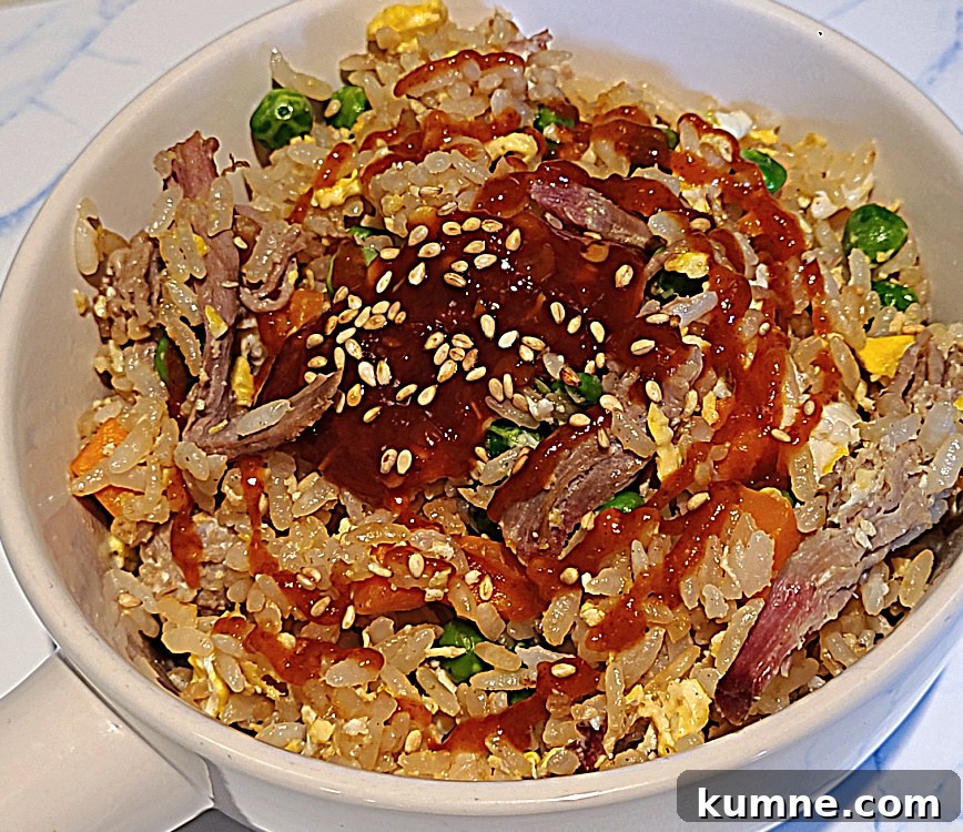 Shredded Pork Fried Rice in a bowl with chili paste, siracha sauce, and sesame seeds on it.