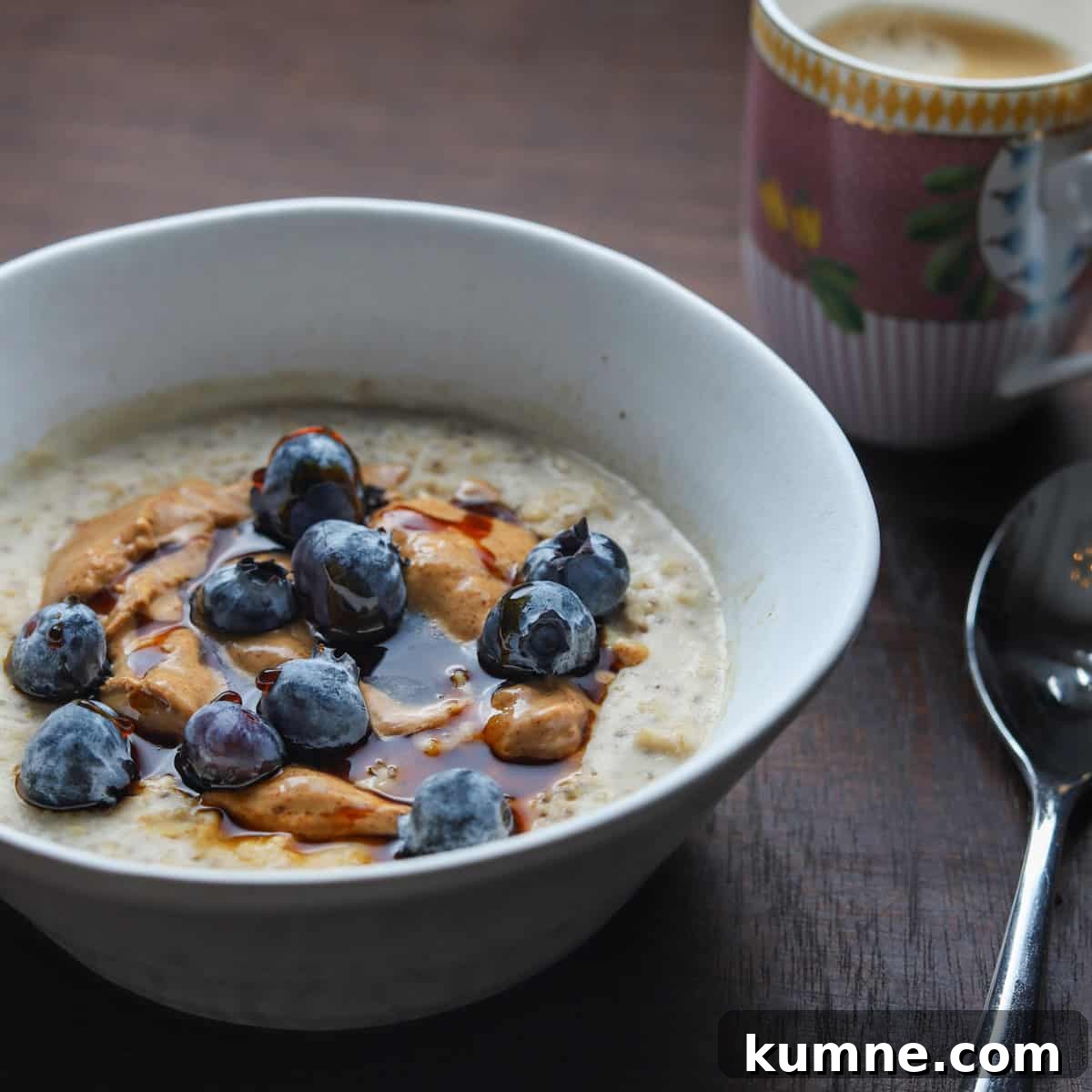 Photo of a bowl of porridge with a coffee and spoon on a wooden table top.