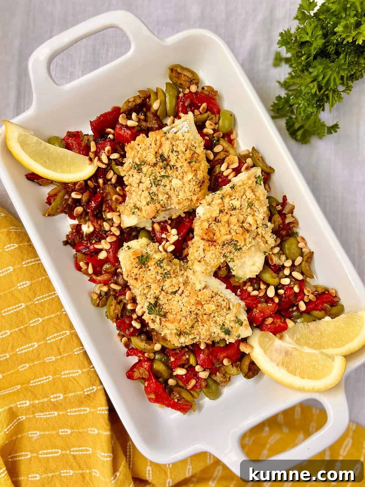 Sicilian Baked Cod in white serving platter garnished with red peppers, olives and lemons.