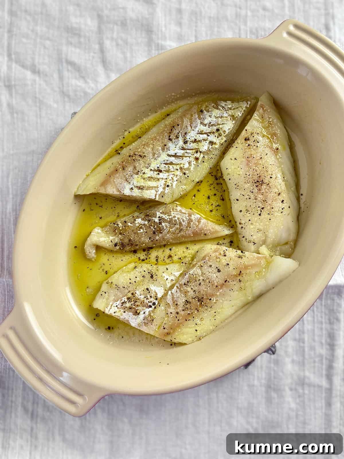 Cod fillets in olive oil in oval baking dish.