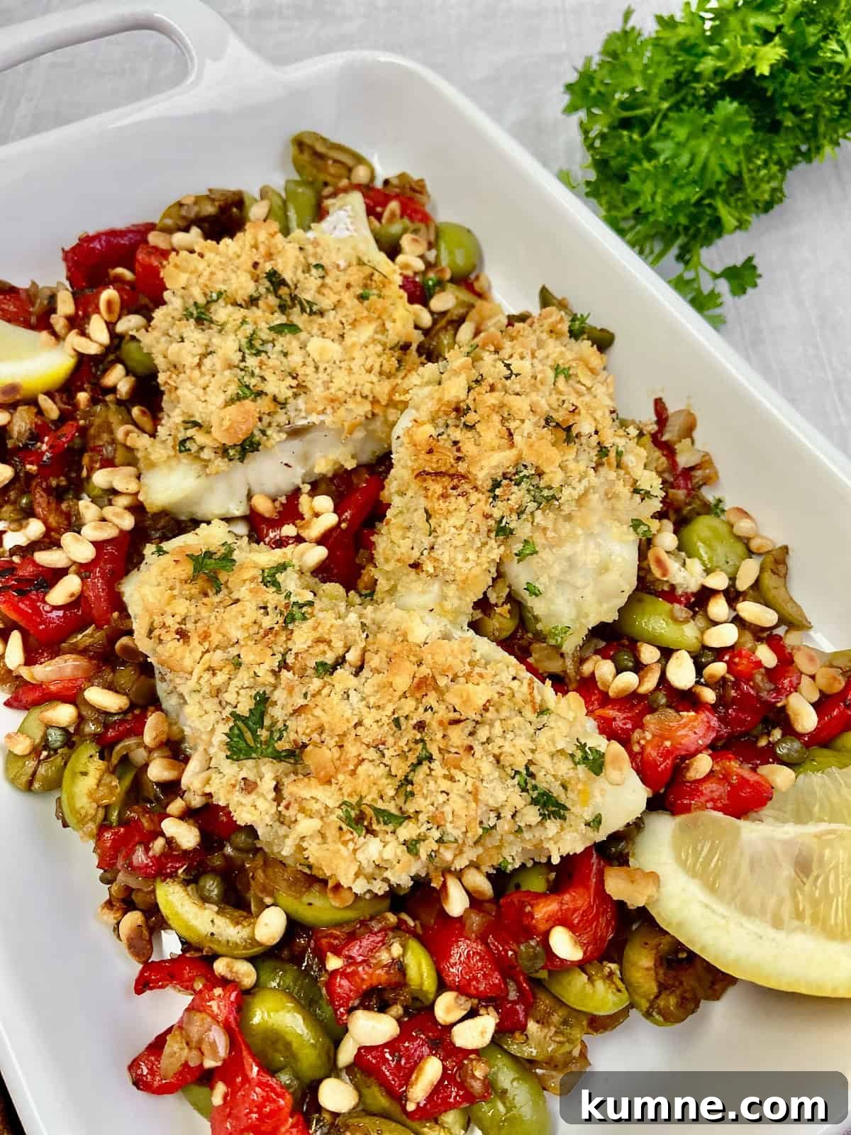Baked cod topped with garlic breading and resting on a bed of roasted red peppers and olives.