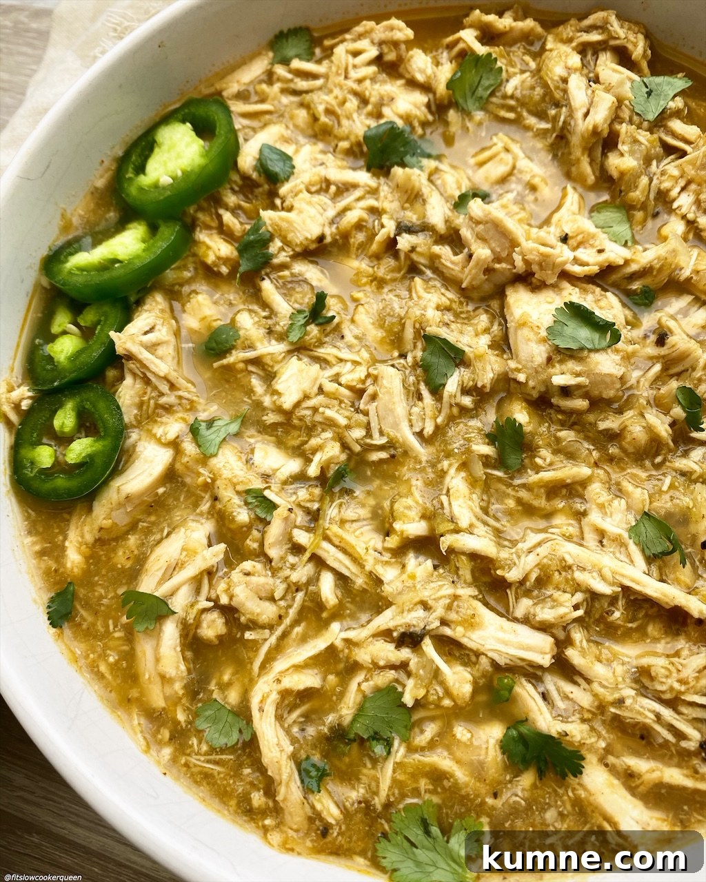 side view of shredded salsa verde chicken in a bowl topped with cilantro & jalapeno