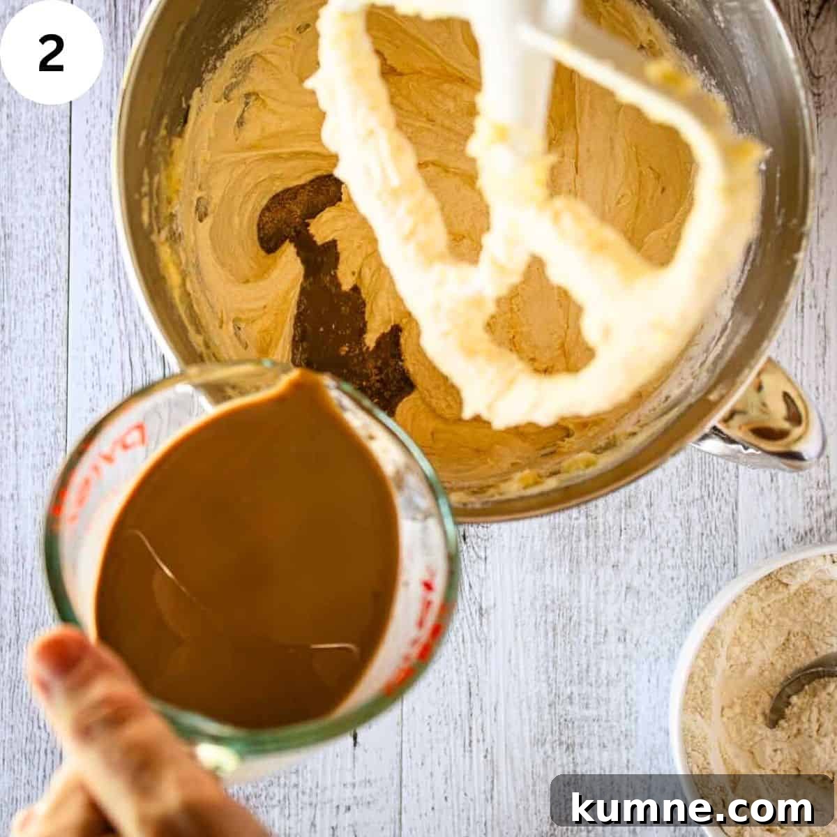 Pouring brown liquid into creamy mixture in a stand mixer bowl.