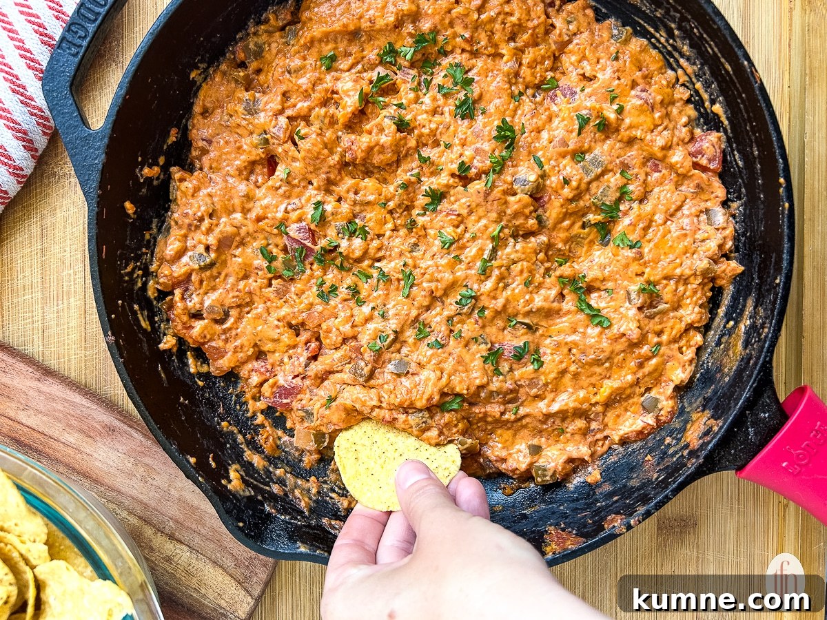 Woman dipping a chip into skillet full of salsa con queso.